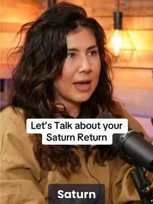 A woman with brown hair and a tan jacket is centered in the frame. The background features a warm, wooden-toned wall accented by a vintage-style light fixture. The primary element is the woman, speaking into a microphone, while overlays announce the video's subject, "Let's Talk about your Saturn Return," and a lower banner stating "Saturn."