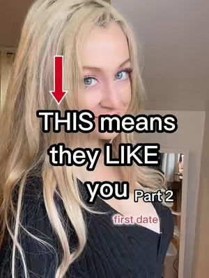 A blonde woman with blue eyes smiles directly at the camera. The video overlayed on the image says "This means they LIKE you Part 2". An arrow points from the top left corner down to the text. Additional text at the bottom says "first date".