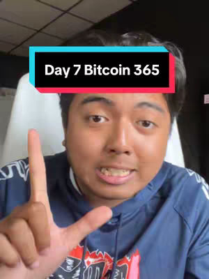 A close-up shot featuring a man in a blue hooded sweatshirt, gesturing with his left hand, holding up two fingers. He is facing the camera, with a text box overlayed on his screen that says 'Day 7 Bitcoin 365' in a bold, sans-serif font.