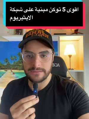 A man in glasses and a black cap with the word 'HERMES' on it, holding a microphone. There's text overlayed on top. The background shows a room with a lamp and some decorative elements.