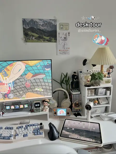 An aesthetically arranged desk space with multiple screens, accessories, and collectibles. The color scheme is neutral with pops of color from the screens and decor, and the overall composition is well-lit and tidy.