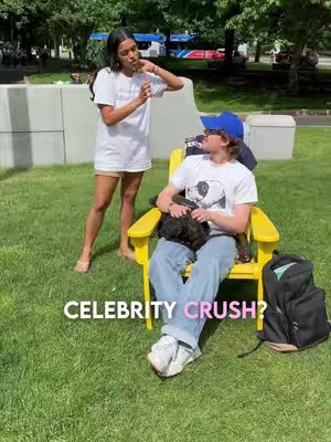 The cover image shows two young people outdoors. A woman is standing, holding a small object near her mouth, and a man is sitting in a yellow chair, holding a small dog. Text at the bottom reads 'CELEBRITY CRUSH?'. The scene is set on a grassy area, with trees and hints of other structures in the background. The lighting appears to be natural, suggesting a daytime shoot.