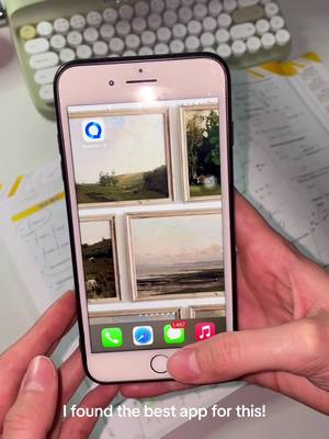 A person is holding a smartphone displaying the QuestionAI app, on top of colorful documents with a keyboard in the background. The phone's screen showcases an app with landscape paintings. The person's hands are visible, holding the phone, with the overlay text at the bottom of the screen.