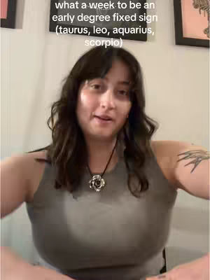 A woman with dark hair and a grey top looks directly at the camera. Text on the background states: 'what a week to be an early degree fixed sign (taurus, leo, aquarius, scorpio)'.