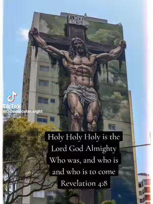 The image showcases a tall building with a mural of Jesus on the cross. The mural is detailed, with visible muscles and a realistic depiction. Text overlayed onto the image states a religious quote with the account handle on the bottom-right.