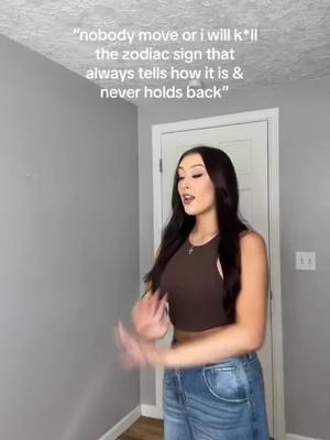 A young woman stands in a room with gray walls and a white door, speaking to the camera. She wears a brown top and blue jeans. Text overlays the image.