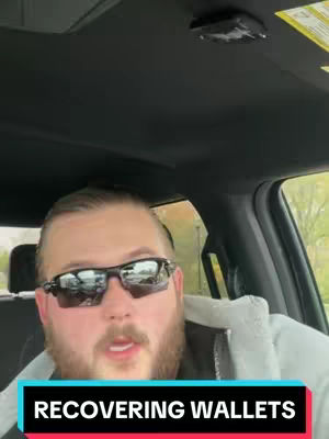 A man wearing sunglasses is sitting in a car, with a text overlay at the bottom of the image that says "RECOVERING WALLETS". The man has a beard and is looking directly at the camera. The car's interior is visible, including the ceiling and a portion of the window. The lighting appears to be from an overcast day.