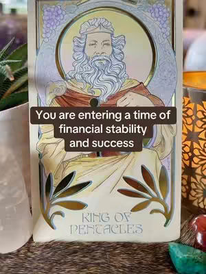 The cover image is dominated by a Tarot card featuring the King of Pentacles. The card has an Art Nouveau style, with an ornate frame surrounding a portrait of a man, presumably the King. He has a long white beard, and is wearing robes. In the background, decorations similar to flowers. The setting also includes a succulent, crystals and lit up candle.