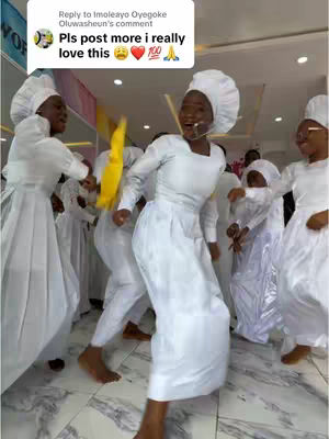 A group of people dressed in white religious attire dancing in a bright, indoor setting. The focus is on a woman in the center who is dancing energetically. Other people are visible in the background, also dressed in white, and the composition is well-lit.