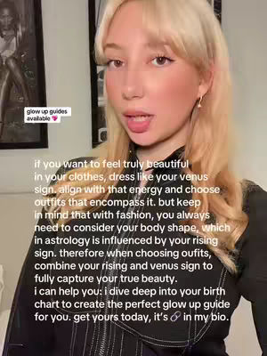 A woman with blonde hair is centered in the frame, looking directly at the viewer and talking. She is wearing a black top. White text is overlayed on the image with a pink heart at the end. Additional text is overlaid on the video. The background includes hints of framed pictures.