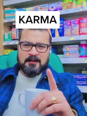 A man in a blue plaid shirt and glasses is holding a white mug, pointing upwards with his right index finger. The background shows shelves stocked with various products.