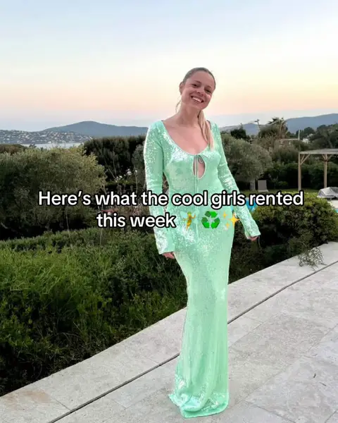 A woman in a long, shimmering green dress stands on a stone surface with greenery and a scenic background of the ocean and distant mountains under a sunset-colored sky. Text overlays read, 'Here's what the cool girls rented this week' and some recycle emojis are included.