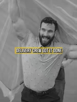 A black and white image with a man as the central focus. He is smiling, holding what appears to be fabric over his head, creating a dynamic, energetic pose. The background suggests an outdoor setting, and the image contains text overlay set against a yellow background.