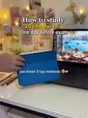 A desk setting with a laptop open on a table. A hand is holding a blue tablet, and there are notes and decorations in the background.