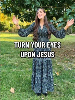 A woman with long brown hair stands outside in a field of green grass and trees. She wears a long-sleeved, dark dress. The overlay text reads 'TURN YOUR EYES UPON JESUS'.