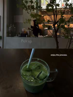 The image is divided into two parts, with a dark wooden table in the foreground and elements of a cafe in the background. The top half features a counter with the text "Pick up" in the center. Behind the counter, someone is visible, and a tree is positioned, partially obscuring the counter. The bottom half shows a glass of green drink with ice cubes, with a straw coming out of it. On the top right of the glass, it's written "enjoy the process."