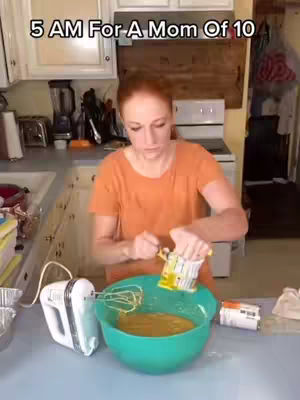 A woman with red hair is in a kitchen at 5 AM, mixing ingredients in a large teal bowl. The scene is brightly lit, with a focus on the cooking process.