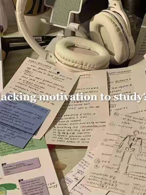 A top-down shot of a cluttered desk with handwritten notes, sticky notes, and open textbooks, with a pair of white headphones resting on top.