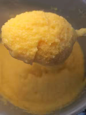 The cover image shows a spoonful of bright yellow, creamy polenta being lifted from a pot. The polenta has a thick, textured consistency. The background is slightly blurred and the overall color palette is warm.