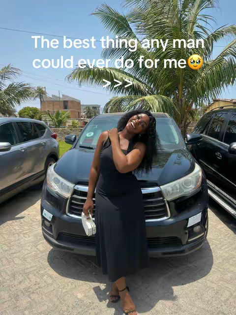 A woman stands in front of a black car, smiling and leaning with her arm on the side of the car. The background includes palm trees and a blue sky. Text is overlaid on the image in a bubble.