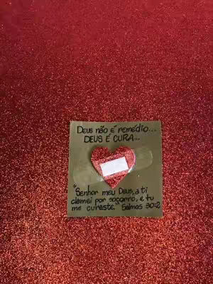 A close-up shot of a square piece of paper with printed text and a red heart with a white bandage on it. The background is a shimmering red surface.