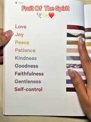 A person holding a book open to a page listing the fruits of the spirit. The page has a title at the top, a dove and a heart symbol. The list of words span one side of the pages along with a striped color coded section.