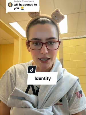 A woman with a headband with bear ears, glasses, and a t-shirt is shown in a close-up shot. She is in a well-lit room, possibly a bathroom, with a banner over her.