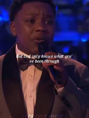 A medium shot captures a young Black man, dressed in formal attire with a bow tie, singing into a microphone. Text overlays the image stating a message of faith. The lighting is dim with blurred background suggesting a stage setting.