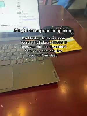 The cover image shows a laptop on a brown wooden surface, possibly a desk. The laptop screen displays what appears to be a financial chart or data, and a black mouse rests beside it. The image has text overlayed that reads, 'Maybe an unpopular opinion: Backtesting for hours upon hours a day helps no trader. It turns you into the \"I wouldn't have done that on a live account\" mindset.' The overall composition is well-lit and focused on the laptop and the surrounding objects.