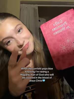 A young woman with long brown hair is holding a pink book, likely a Bible. She's looking towards the camera and pointing with her index finger, while the text overlay says that she's raising a Hispanic man of God.
