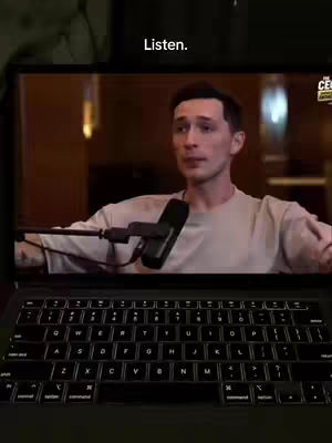 A laptop displaying a video of a man speaking. The man is shown in the screen, with a microphone in front of him.