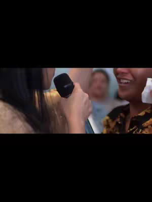 The cover photo shows a close-up shot of two women. The woman on the left is holding a microphone close to the woman on the right. The woman on the right is smiling and holding a white tissue. In the background, another person's face is visible.