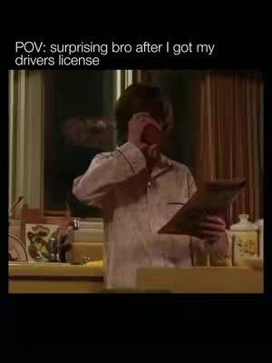 The image shows a person in pajamas reacting to something. They are holding a paper and covering their mouth with their hand. Kitchen is visible in the background.