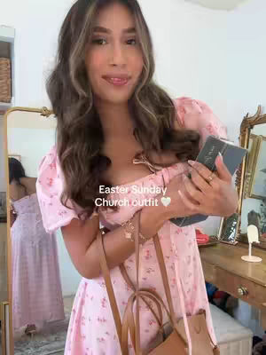 A woman in a pink floral dress poses with a phone in front of a mirror. Text overlay reads 'Easter Sunday Church outfit'. The background includes a glimpse of a church setting, a gold mirror and a wooden table.