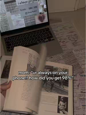 The cover image shows a laptop open with a grade of 100/100 displayed and a textbook with a black and white illustration. The text overlay at the bottom reads "mom: "ur always on your phone!! how did you get 98%"". The shot includes pages of notes and paper scattered around the laptop and book, suggesting a study environment.