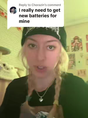 A young woman with blonde braids wearing a black beanie and a black shirt is centered in the frame. She is speaking with an open mouth. A text bubble with the comment "I really need to get new batteries for mine" by Chorazin's shows up near the top left of the screen.
