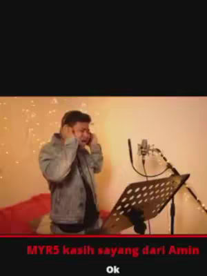 The cover image shows a man wearing a gray jacket with headphones on. He is looking down and appears to be singing into a microphone. A music stand rests in front of him, and behind him are lights that look like fairy lights. Text overlays at the bottom in red read "MYR5 kasih sayang dari Amin ok".