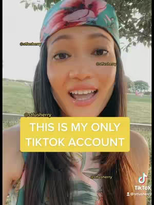 A woman with long dark hair is the central figure, smiling and facing the camera directly. She's wearing a colorful headscarf and a top with a floral pattern. A yellow banner with text overlays her body. The background is blurred, suggesting an outdoor setting.