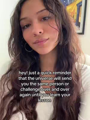 A selfie-style video featuring a young woman with long, wavy brown hair. She's looking slightly upwards with a soft expression. Text overlayed in a white font provides a quote about the universe sending lessons.