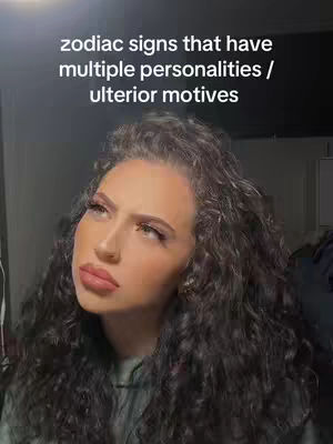 A woman with long curly dark hair looks up slightly with a pensive expression, her face reflecting a shadowed light. Her full lips are slightly parted. Overlay text at the top reads: 'zodiac signs that have multiple personalities / ulterior motives'. Dark background with blurred shadows.