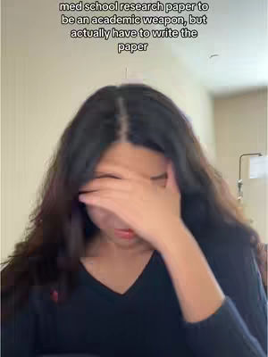 A young woman with long, dark hair covers her face with her hand, conveying a sense of stress. Text overlays at the top indicate the video's theme of research papers and graduate school struggles. The background appears to be a neutral-colored interior.