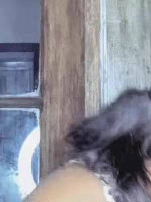 The shot features a person's dark hair and shoulder, partially obscuring the view. The background includes a wooden panel and part of a window frame. The focus is somewhat blurred, suggesting a quick, casual capture.