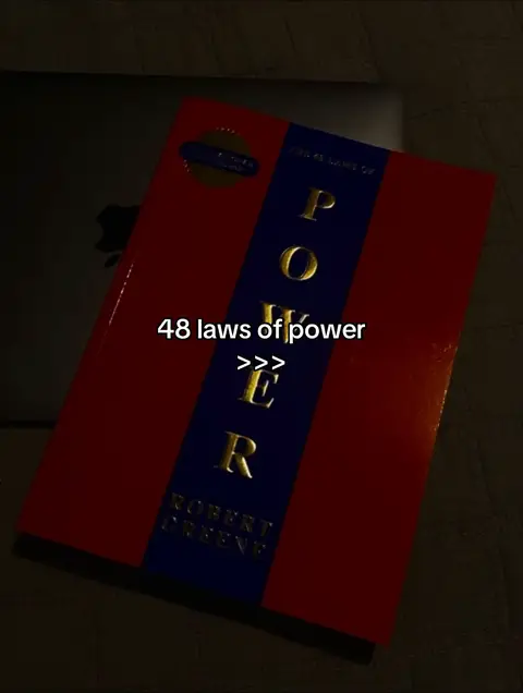 The cover image shows a book titled 'POWER' with the author's name, Robert Greene. The book has a red cover with a blue vertical stripe down the center. The word 'POWER' is written in gold lettering on the blue stripe. At the bottom a laptop can be viewed behind the book on a dark surface.