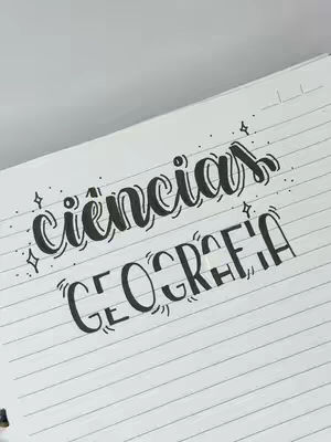 The image shows a close-up of an open notebook, angled diagonally. Two handwritten titles are displayed on the lined paper within the notebook. The letters are crafted in a black, bubbly font. The top title reads "ciências" and "geografia", both decorated with small star-like symbols, and the name is written under the first one.