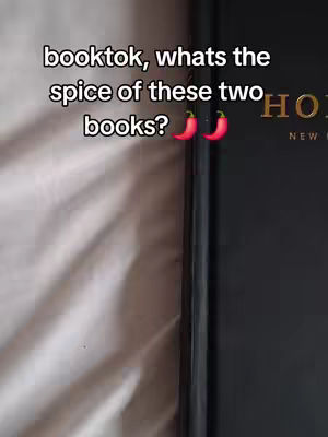The image showcases a close-up of two books resting on a light-colored, slightly wrinkled surface, possibly a bedsheet. The book on the right is mostly black with the gold lettering. The hook text is white and positioned on the top left of the frame.