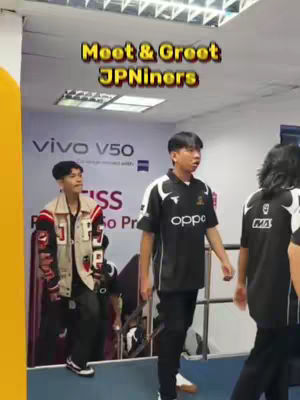 The image shows a crowded indoor setting with three young men as the main subjects. The man on the left is wearing a jacket. The man in the middle is dressed in a black Oppo shirt with black pants. The background includes a Vivo advertisement, and text overlays at the top promoting the event ‘Meet & Greet JPniners’ in yellow and pink.