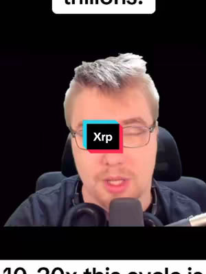 A man with glasses and a dark shirt is centered in the frame, against a dark background. His eyes are covered by a rectangle that has 'Xrp' written in it. The man is speaking into a microphone, with a headset around his neck.