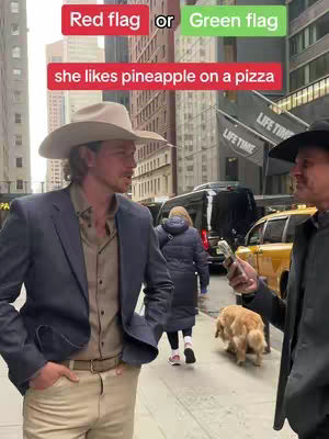 An urban street scene featuring two men in conversation. The main subject is wearing a cowboy hat, a navy blazer, and khaki pants, with his right hand in his pocket. Another man in a black hat and jacket stands to his right, holding a phone up. A tan dog is walking on the right. In the background, there is a city street with tall buildings, cars, a woman in a winter coat, and text overlays at the top of the image.