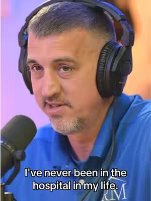 A man with short hair and a beard is wearing headphones and a blue shirt, with a microphone to his left and text overlaying the bottom of the image.