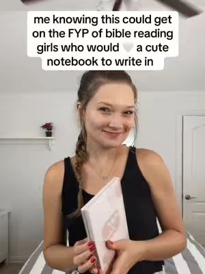 A woman in a black tank top holds a white journal, smiling. A text overlay in a white box above the woman reads: "me knowing this could get on the FYP of bible reading girls who would a cute notebook to write in." The background has a blurred room setting.